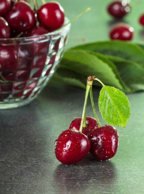 Üç tatlı ıslak dut, kiraz kasesinin yanında, gri yüzeyde.