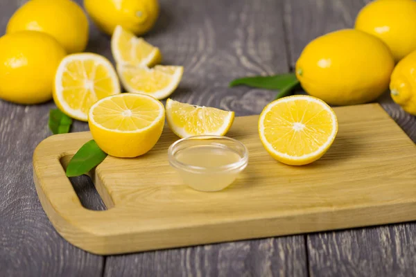 Lot of whole lemons and pieces, bowl of lemon juice on cutting Board — Stock Photo, Image