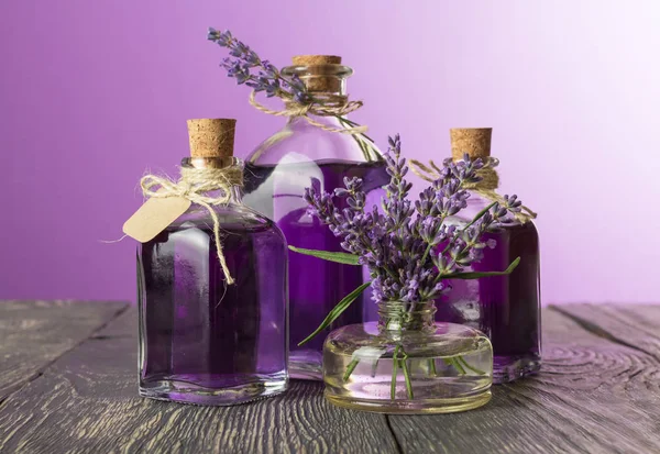 Flaskor med dekokt och lavendel tinktur med proppar och etikett, blommor i vas, på bordet — Stockfoto