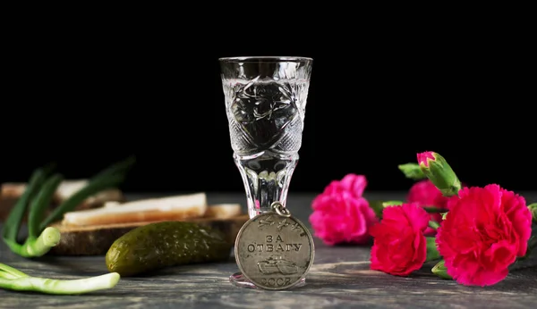 Медаль за доблесть, красные гвоздики и стакан водки, выделенные на черном фоне — стоковое фото