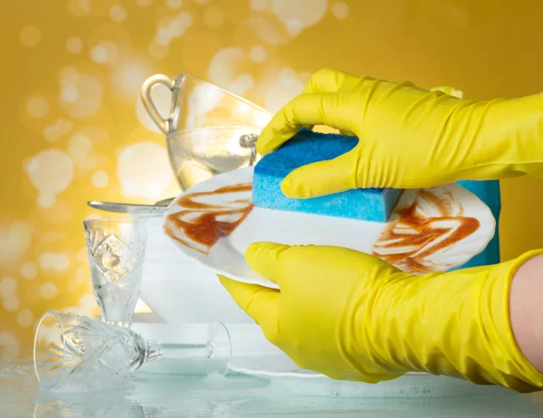 As mãos de mulher em luvas lavam pratos sujos com detergente no amarelo — Fotografia de Stock