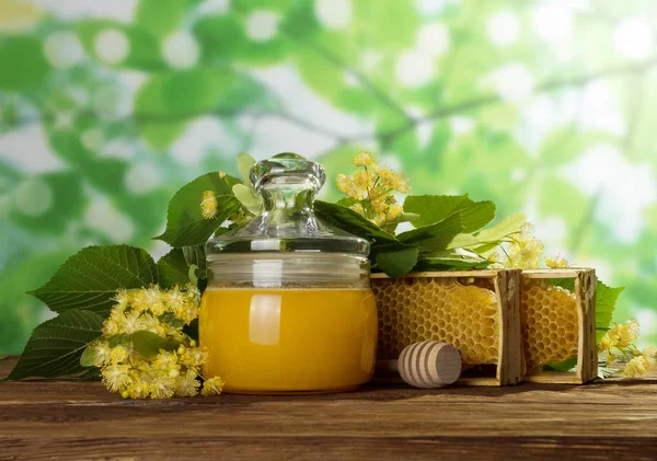 In vaso con coperchio miele fresco, accanto a nido d'ape e fiori sul tavolo di legno — Foto Stock