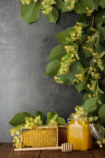 Vaso con miele, nido d'ape e agitatore su sfondo grigio, in cima al ramo di tiglio — Foto Stock