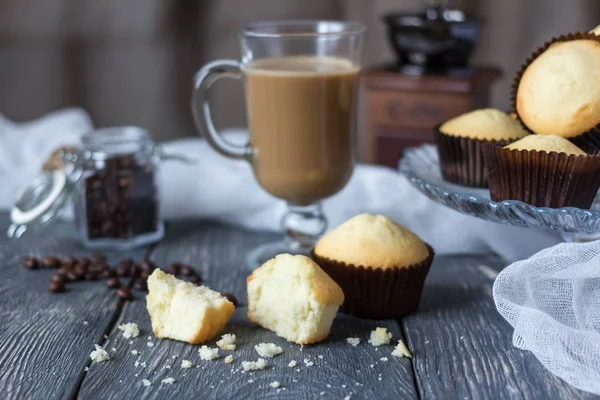 Viele ganze Cupcakes und Stücke auf Holztisch, neben Glasbecher mit Cappuccino — Stockfoto