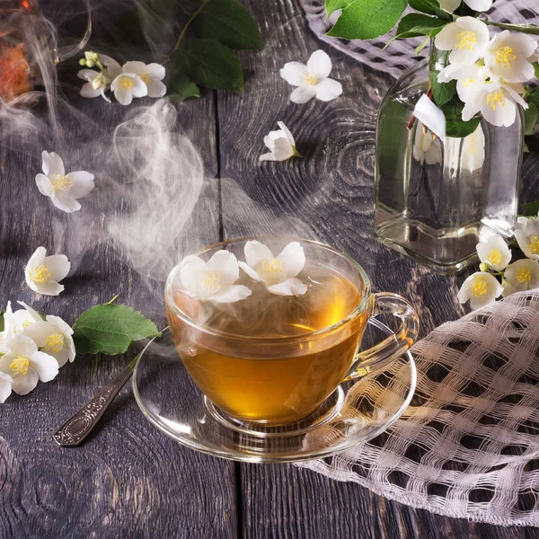 Cup of fragrant hot tea with Jasmine and fresh flowers, on wooden surface — Stockfoto