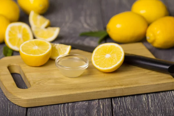 Pieces of lemon and knife on cutting Board, juice in bowl — Stock Photo, Image