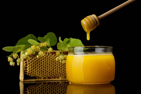 Miele fresco raccolto in primavera nel barattolo, accanto a cucchiaio di legno e telaio isolato su nero — Foto Stock