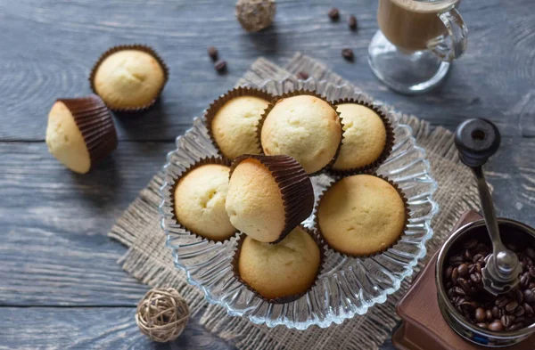 Em prato de vidro de mesa com cupcakes, ao lado de moedor de café mão e xícara de cappuccino — Fotografia de Stock