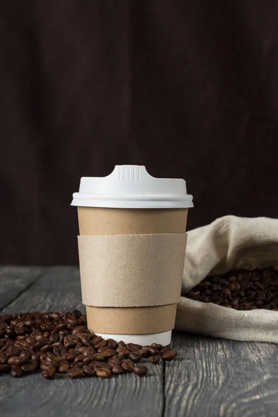 Sklenice kávy, kávová zrna vypadávají z tašky na černém pozadí — Stock fotografie