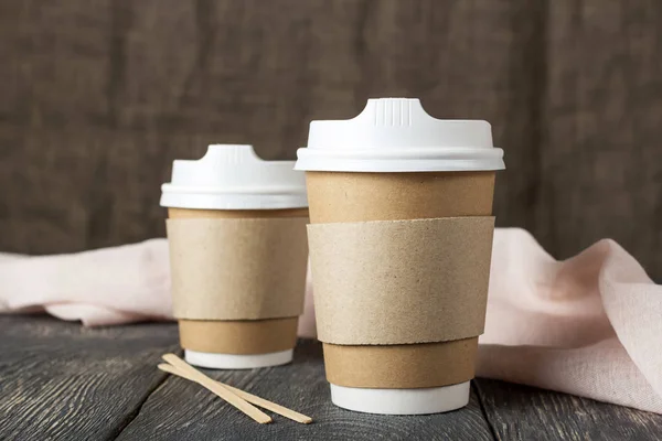 Twee wegwerpbekers met koffie en houten roerstaafjes naast lichte doek op tafel — Stockfoto