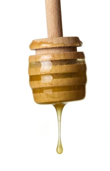 Druppel vloeibare goudkleurige honing stroomt naar beneden met houten roerder geïsoleerd op wit — Stockfoto