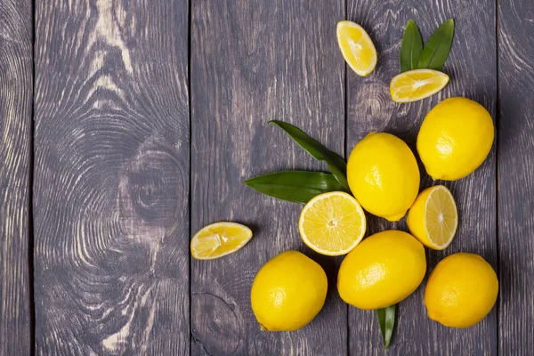 Pocos limones amarillos maduros y trozos cortados en rodajas sobre una superficie vieja — Foto de Stock