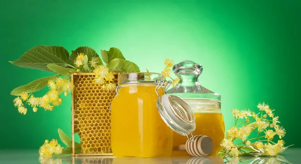 Bancos com mel, favo de mel, fuso de madeira e flores de tília em verde — Fotografia de Stock
