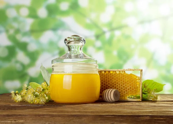 Glass jar of honey, honeycomb and Linden flowers on light green — Stock Photo, Image