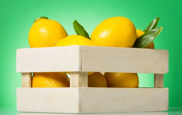 Holzschachtel mit Zitronen auf grünem Hintergrund — Stockfoto