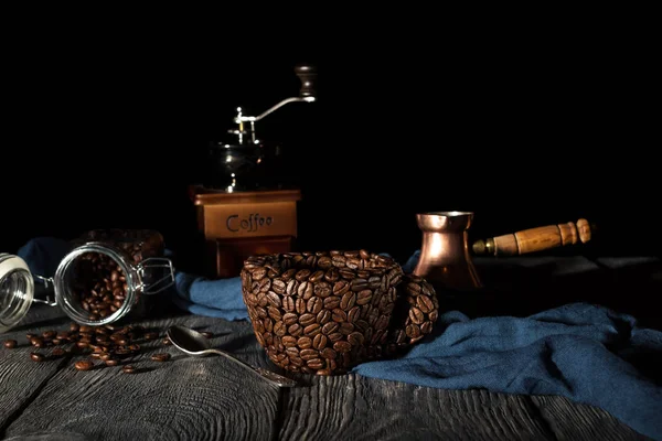 Kahve çekirdeğinden yapılmış bir kupa, mavi kumaşta el değirmeni, siyah üzerine izole edilmiş. — Stok fotoğraf