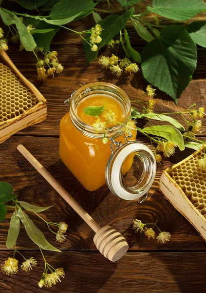 Linden honey in jar, wooden beater and linden flowers on wooden surface — Stock Photo, Image