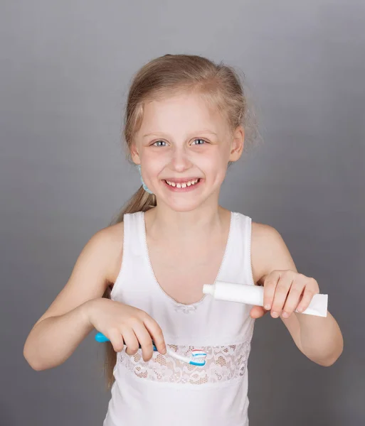 Glimlachend klein meisje poetst haar tanden op een grijze achtergrond — Stockfoto