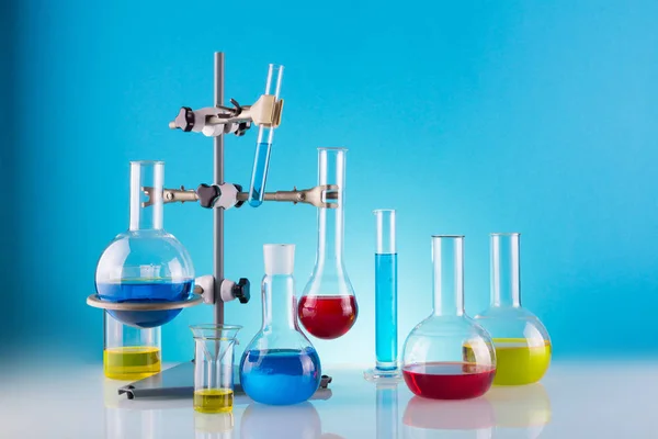 Биологическая лаборатория. Штатив с различными химическими стеклами и цветными жидкостями на синем фоне — стоковое фото