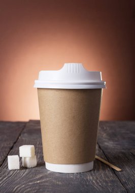 Container-thermos for coffee, near pieces of sugar and stick for stirring, on wooden surface
