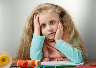 Sad sick girl with scarf sitting at table, next to medicine and inhaler