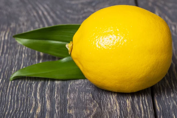 Große leuchtend gelbe Zitrone mit Blättern liegt auf Holzoberfläche — Stockfoto