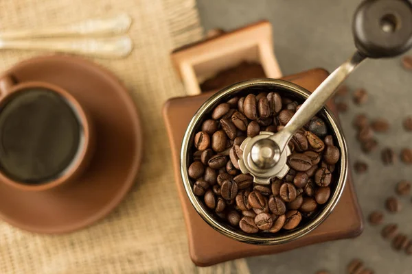 Mill kahve çekirdekleri ile dolu, bir fincan sıcak kahvenin yanında. — Stok fotoğraf