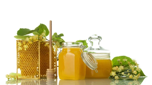 Two jars of honey, frames with honeycombs and spoon, next to Linden flowers, isolated on white — Stock Photo, Image