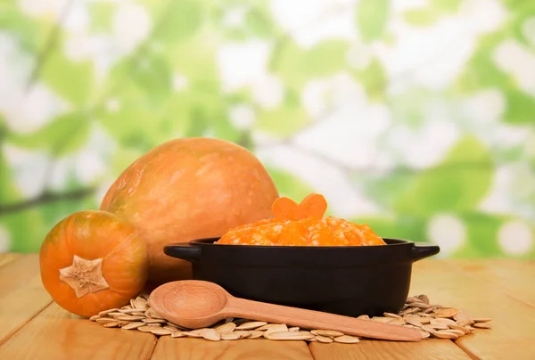 Большая оранжевая тыква, каша в миске, на столе семена тыквы и ложка — стоковое фото