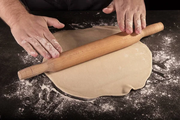 Thin layer of dough, rolling pin in Baker's hands, isolated on black — Stock Photo, Image