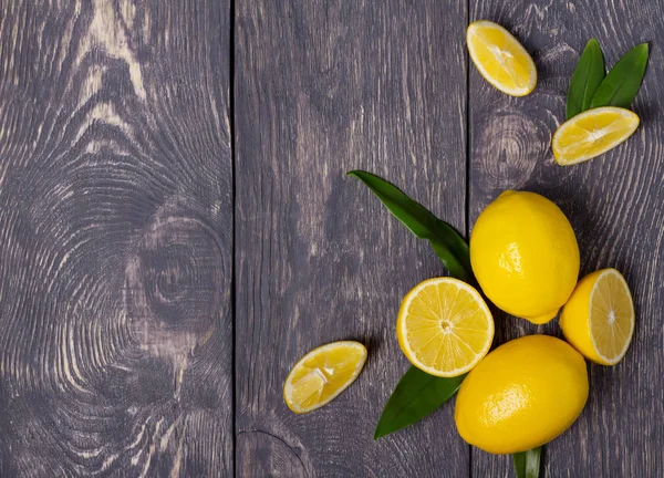 Ganze Zitronen mit Blättern und in Stücke geschnitten, auf Holzoberfläche — Stockfoto