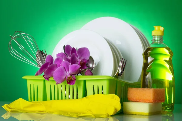 Clean plates and Cutlery in dryer, detergent, sponges and gloves, on green — 图库照片