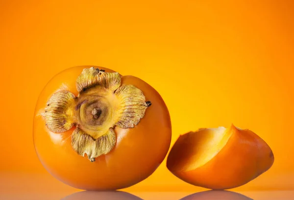 Fruta inteira de cáqui e pedaço cortado, sobre fundo laranja — Fotografia de Stock