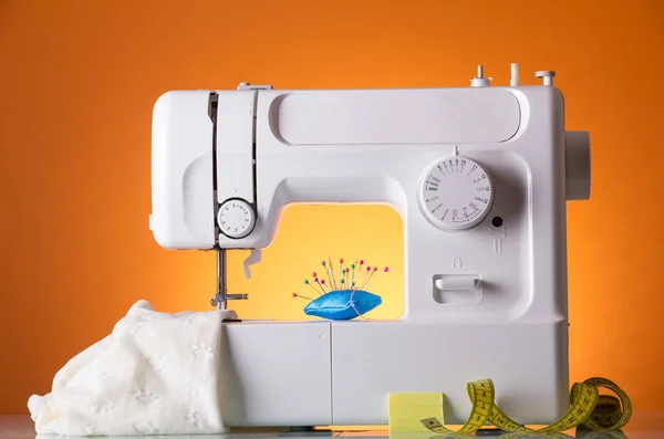 Sewing machine, fabric under sewing foot, pillow with needles and centimeter, on orange background — Φωτογραφία Αρχείου