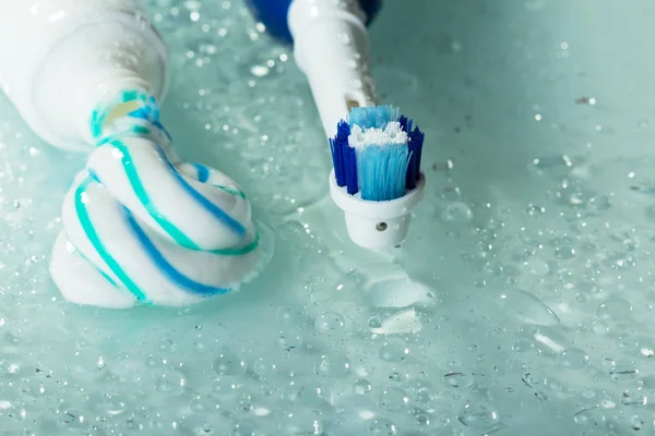 Electric toothbrush and paste, fallen out of tube, on wet shelf — Stock Photo, Image