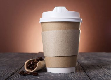 Kahve için kapağı olan özel bir konteynır, masa üzerinde kahve çekirdekleri olan ahşap kepçenin yanında.