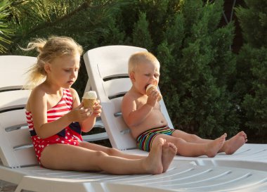 Denizde yaz tatili, çocuklar şezlongda oturarak dondurma yiyor.