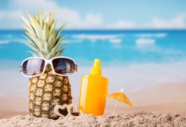 Ananas, güneş gözlüğü, şemsiye ve güneş kremi, kumlu sahilde.