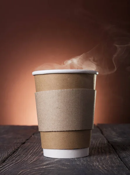 Disposable Cup of steaming hot coffee on dark wooden table