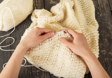 İşinde ustanın elleri, iplik, örgü iğneleri ve koyu ahşap arka plandaki bitmiş ürün.