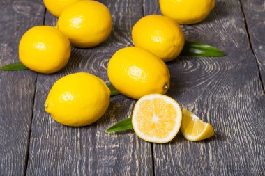 Parlak sarı limonlar ve parçalar koyu ahşap yüzeye saçılmış. Yakın çekim.