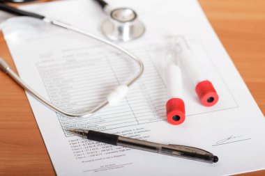 Kan, fonendoskop, kalem ve muayene sonuçları masada.