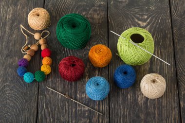 Farklı renklerde iplikler ve karanlık ahşap yüzeyde zanaat için kancalar.
