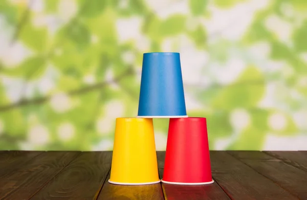 三个五颜六色的塑料杯倒立在一张褐色的木制桌子上 — 图库照片