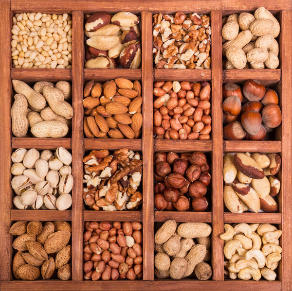Large selection of peeled nuts, and kernels in shell, in wooden box with cells. Background
