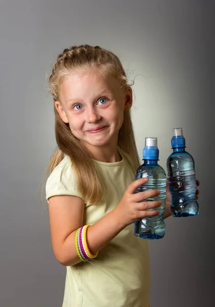 Две Бутылки Чистой Воды Руках Маленькой Улыбающейся Девушки Сером Фоне — стоковое фото