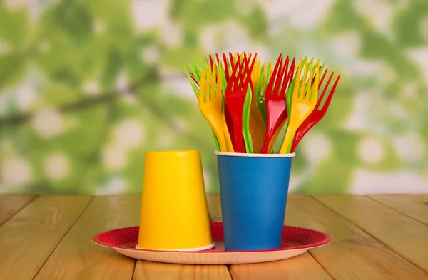 多色使い捨てフォークは ベージュの木製テーブルの上に プレート上のプラスチックカップに立つ — ストック写真