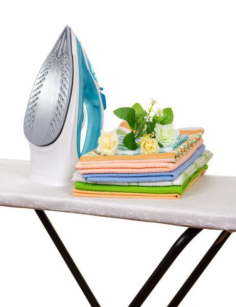 Electric iron, stack of towels and bouquet on an ironing board isolated on white background