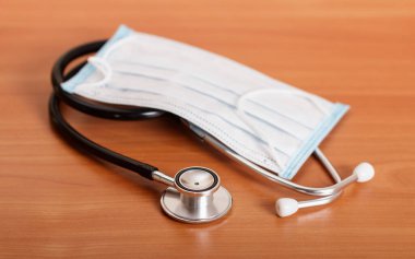 Kahverengi masanın arka planına karşı bireysel koruyucu maske ve fonendoskop