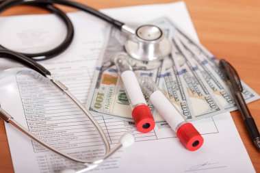 Phonendoskop, kan testi tüpleri, anket sonuçları ve masa arkasındaki para.